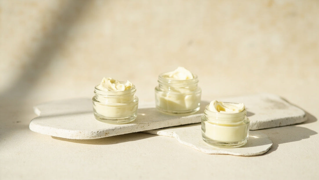 Three glass jars of creamy skincare cream on stone trays, natural light, clean beauty