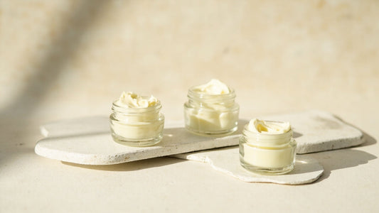 Three glass jars of creamy skincare cream on stone trays, natural light, clean beauty